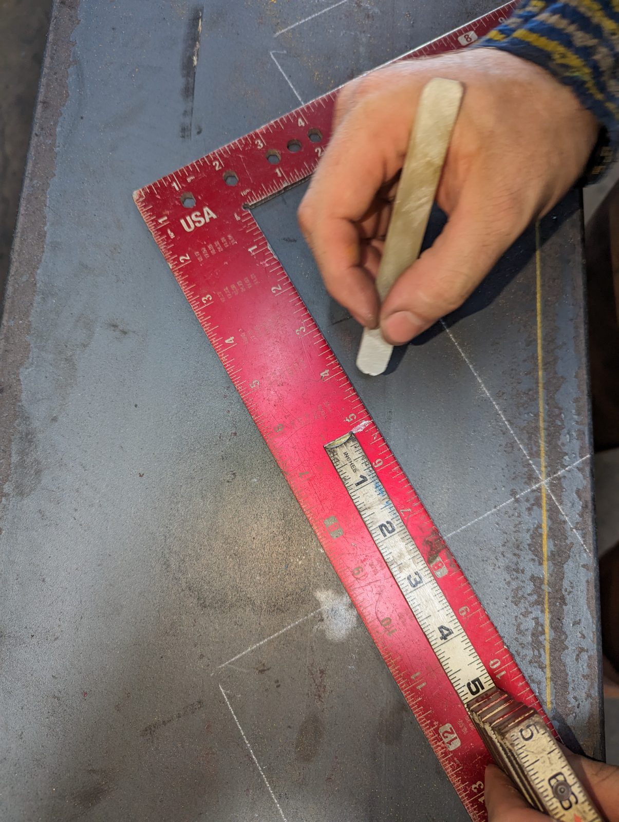 Soapstone and a framing square marking a layout line on steel plate